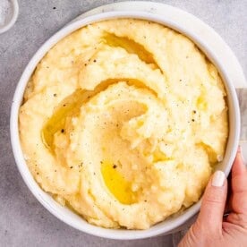 Creamy mashed potatoes served in a white bowl with melted butter swirled on top.