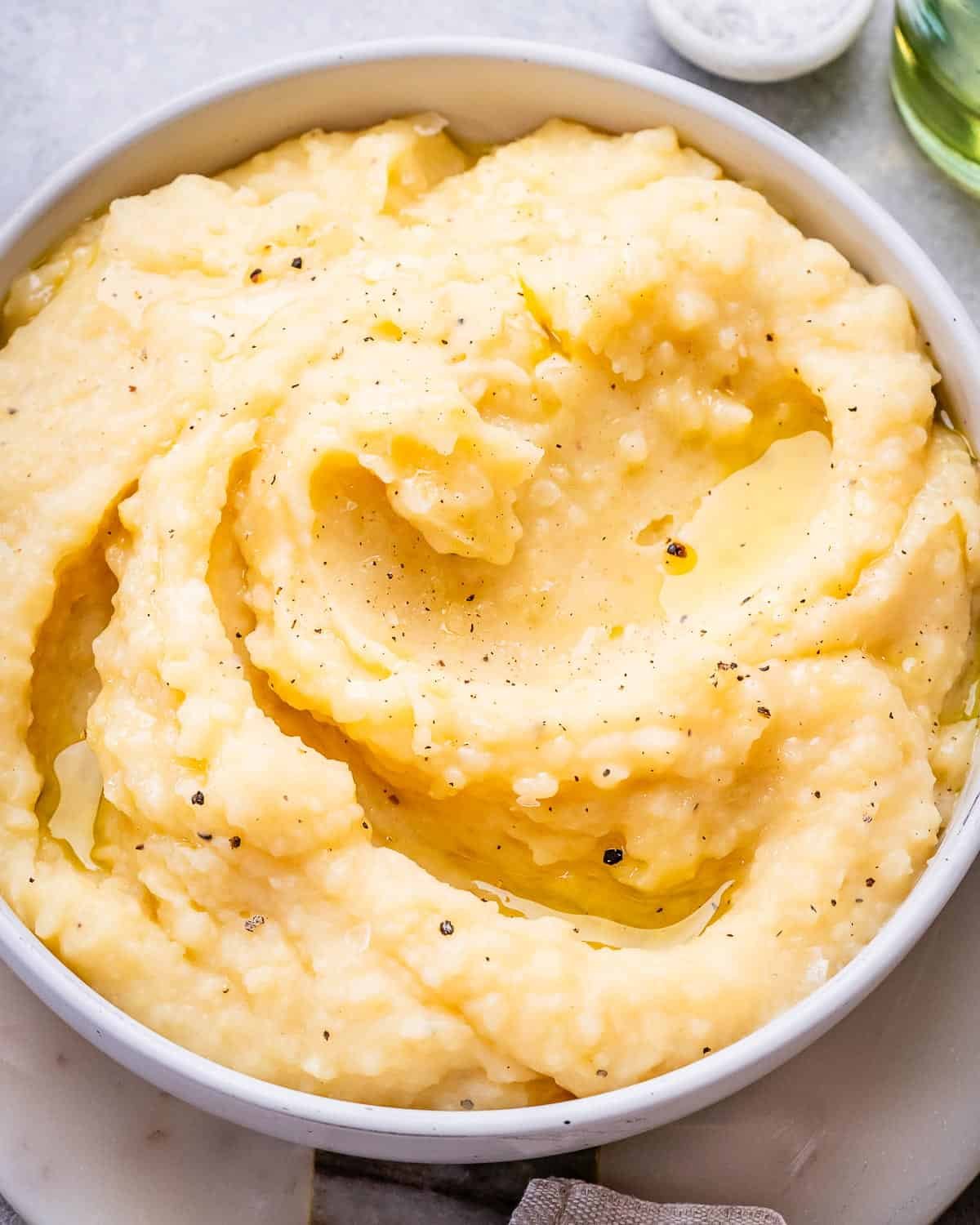 Fluffy mashed potatoes in a bowl, seasoned with black pepper and drizzled with butter.