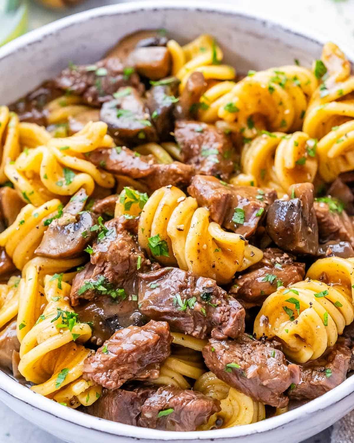 Close-up of cooked beef stroganoff with tender beef, mushrooms, and pasta coated in a creamy sauce.
