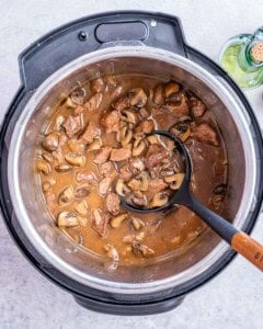 Rich mushroom sauce simmering eith beef in the Instant Pot with a ladle resting inside.