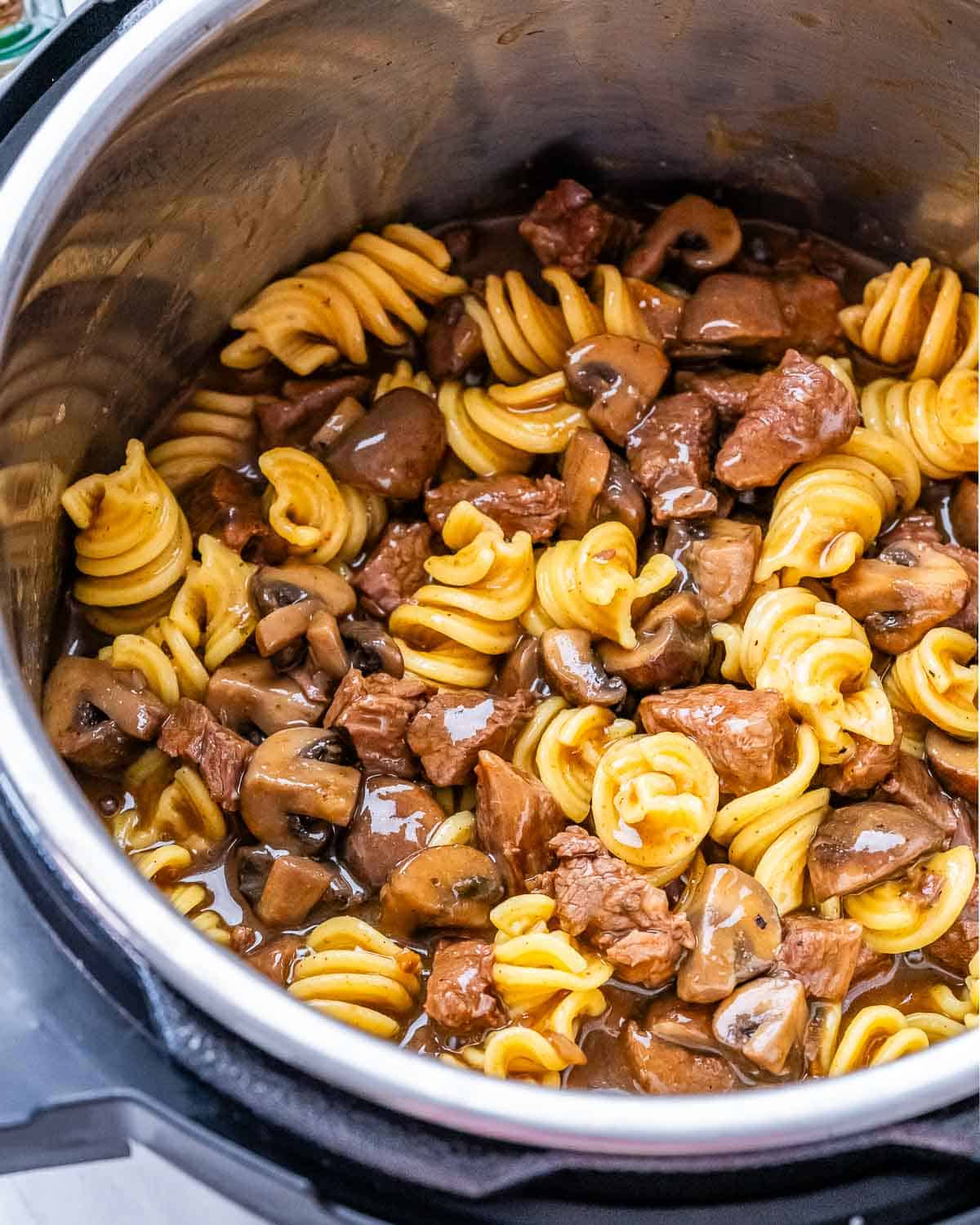 Pasta, beef, and mushrooms cooking together in the Instant Pot, almost ready to serve.