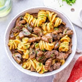 Freshly cooked stroganoff in a white bowl with rotini pasta, beef, and mushrooms mixed together.