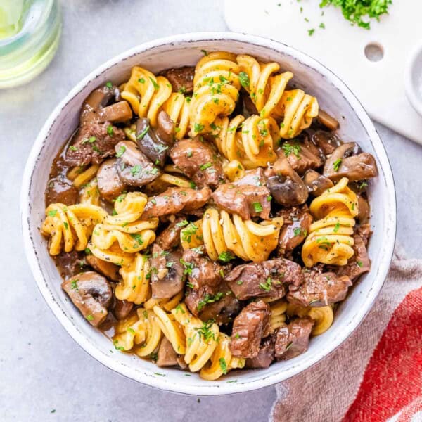 Freshly cooked stroganoff in a white bowl with rotini pasta, beef, and mushrooms mixed together.