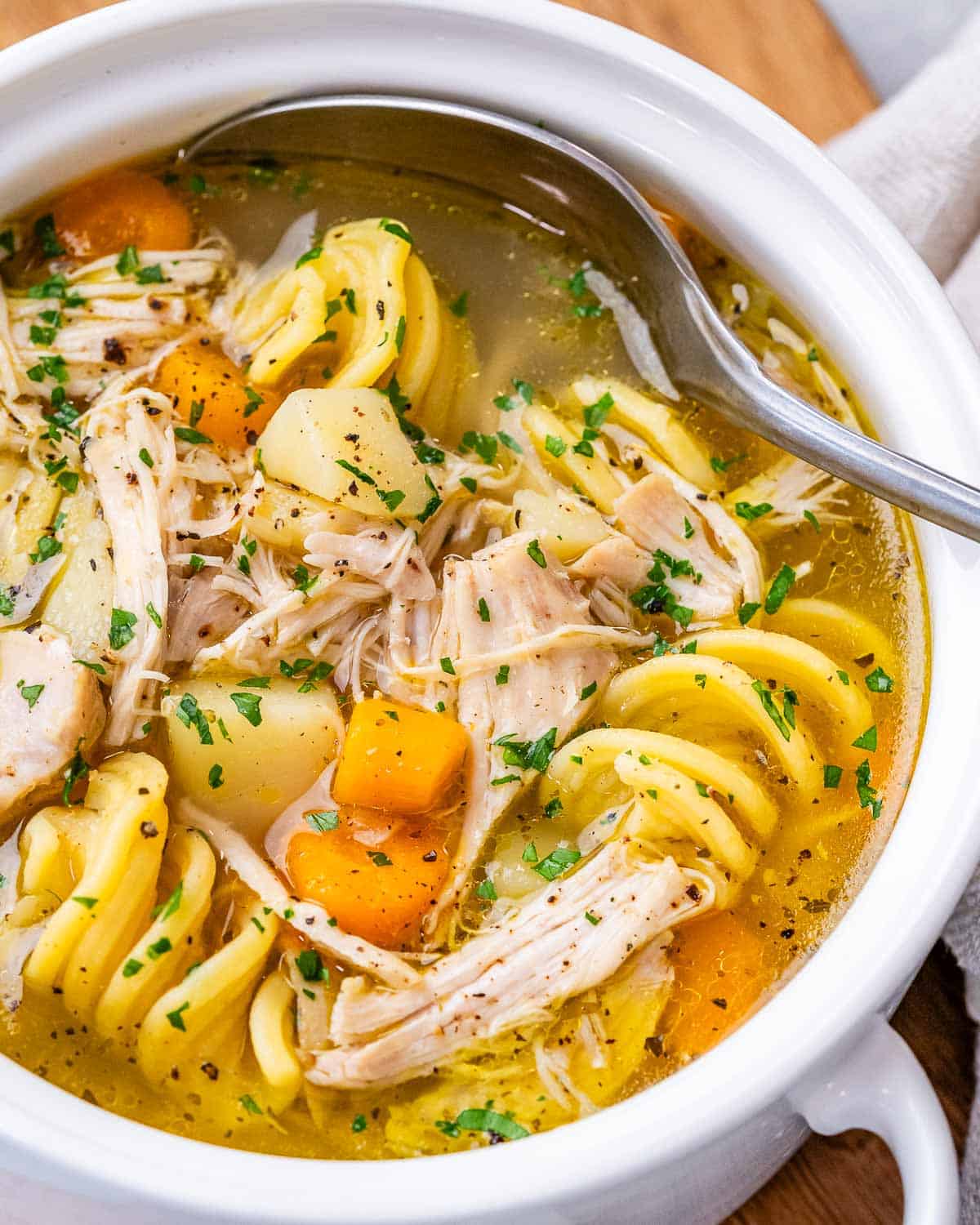 Overhead view of a steaming bowl of chicken noodle soup, garnished with fresh parsley and filled with hearty vegetables.