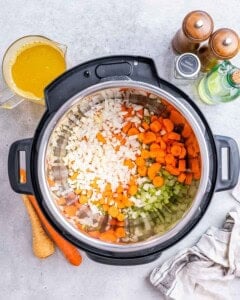 Diced onion, celery, and carrots being sautéed inside the Instant Pot with broth nearby.