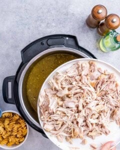 Shredded chicken on a plate being returned to the Instant Pot filled with soup broth.