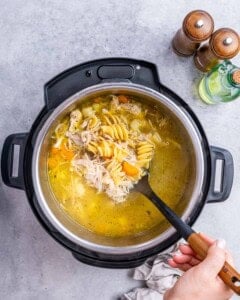 Instant Pot filled with hot broth and noodles being stirred with a ladle.