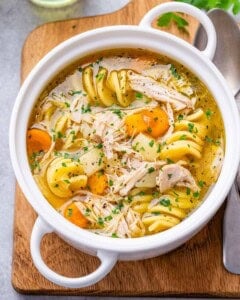 A white bowl filled with homemade Instant Pot chicken noodle soup, loaded with carrots, potatoes, and rotini noodles.