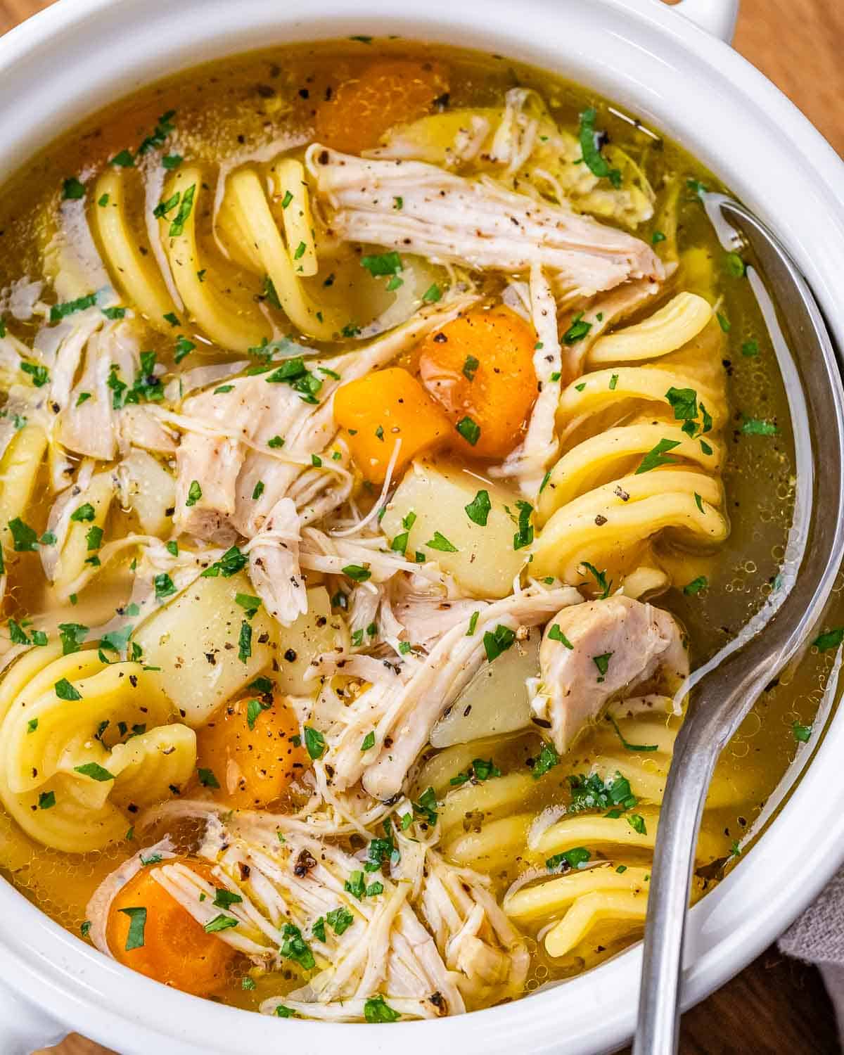 Close-up of chicken noodle soup in a white bowl, showing shredded chicken, bright orange carrots, and tender potatoes in broth.
