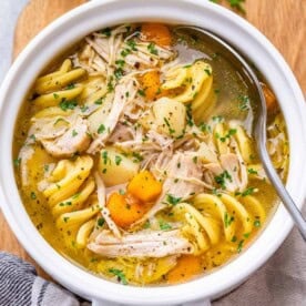 Close-up top view of chicken noodle soup in a bowl, highlighting the golden broth, egg noodles, and chunks of chicken.