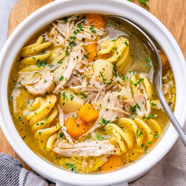 Close-up top view of chicken noodle soup in a bowl, highlighting the golden broth, egg noodles, and chunks of chicken.