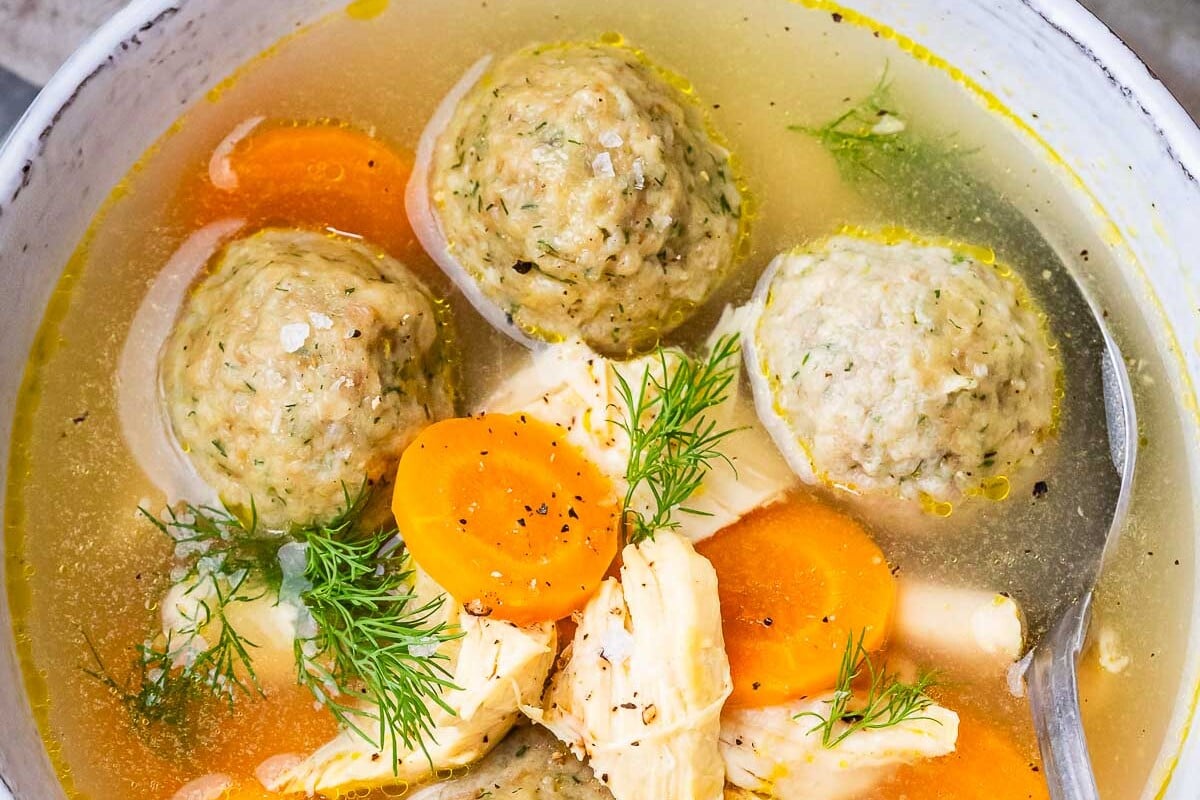 A closeup of matzo ball soup in a white bowl