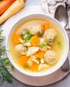 A white bowl of matzo ball soup with a spoon