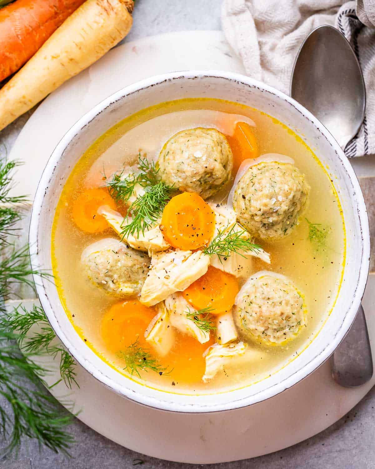 A white bowl of matzo ball soup with a spoon