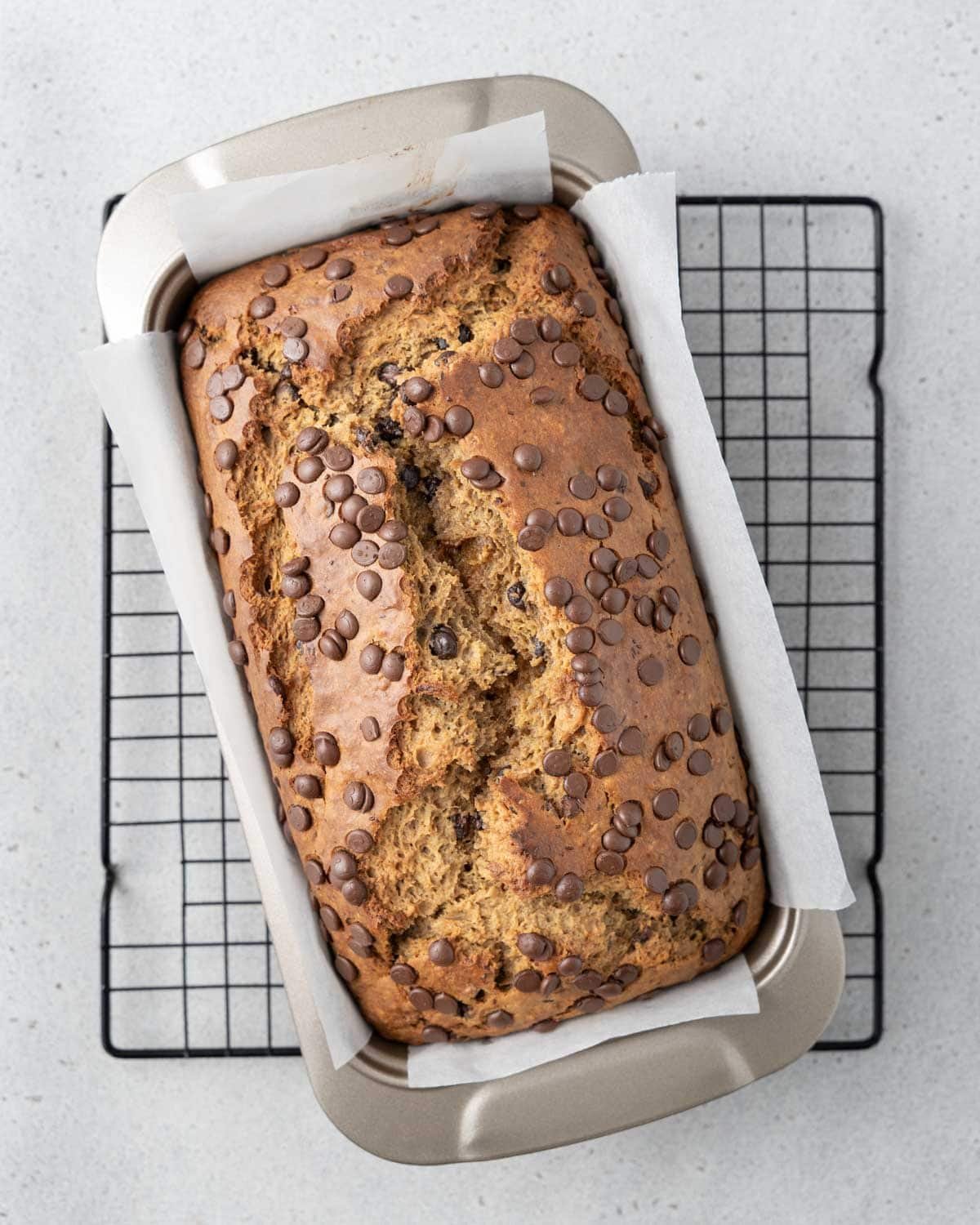 banana bread in a pan on a wire rack.