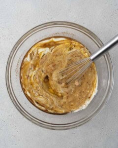 mashed banana, yogurt, egg, oil, and sugar are added to a bowl to be mixed for banana bread.