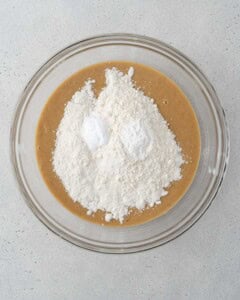 flour added over the wet mixture in a bowl for banana bread.