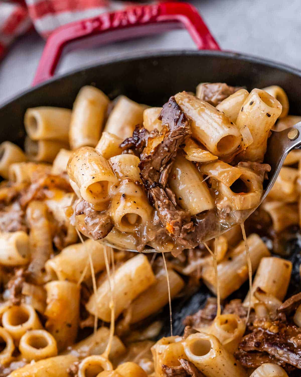 A spoonful of Philly cheesesteak pasta with melted provolone