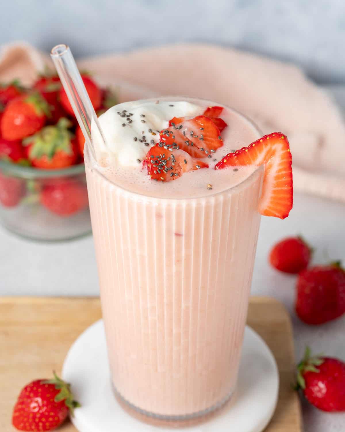 a glass filled with strawberry shake topped with sliced strawberries, chia seeds, and whipped cream.