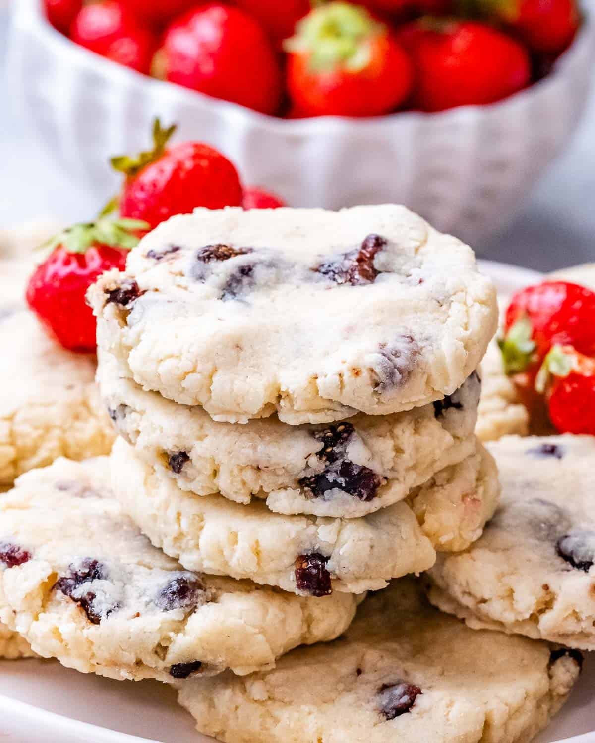 A stack of soft strawberry cheesecake cookies on a plate with fresh strawberries in the background.