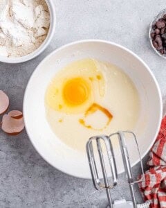 Egg and vanilla added into the wet mixture, with a hand mixer nearby ready to blend.