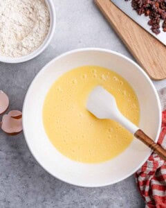 Light yellow wet ingredients mixture in a bowl being stirred with a spatula.