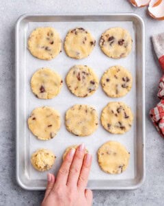 A hand pressing down dough balls on a baking sheet before baking.