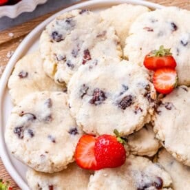 Overhead shot of cookies piled onto a white plate with whole strawberries on the side.
