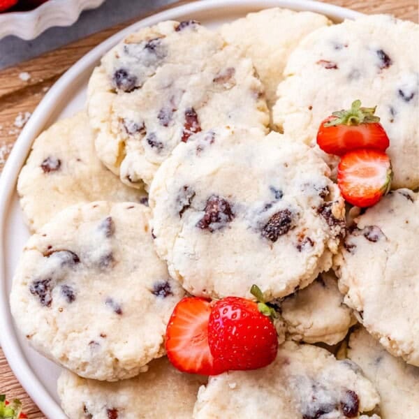 Overhead shot of cookies piled onto a white plate with whole strawberries on the side.