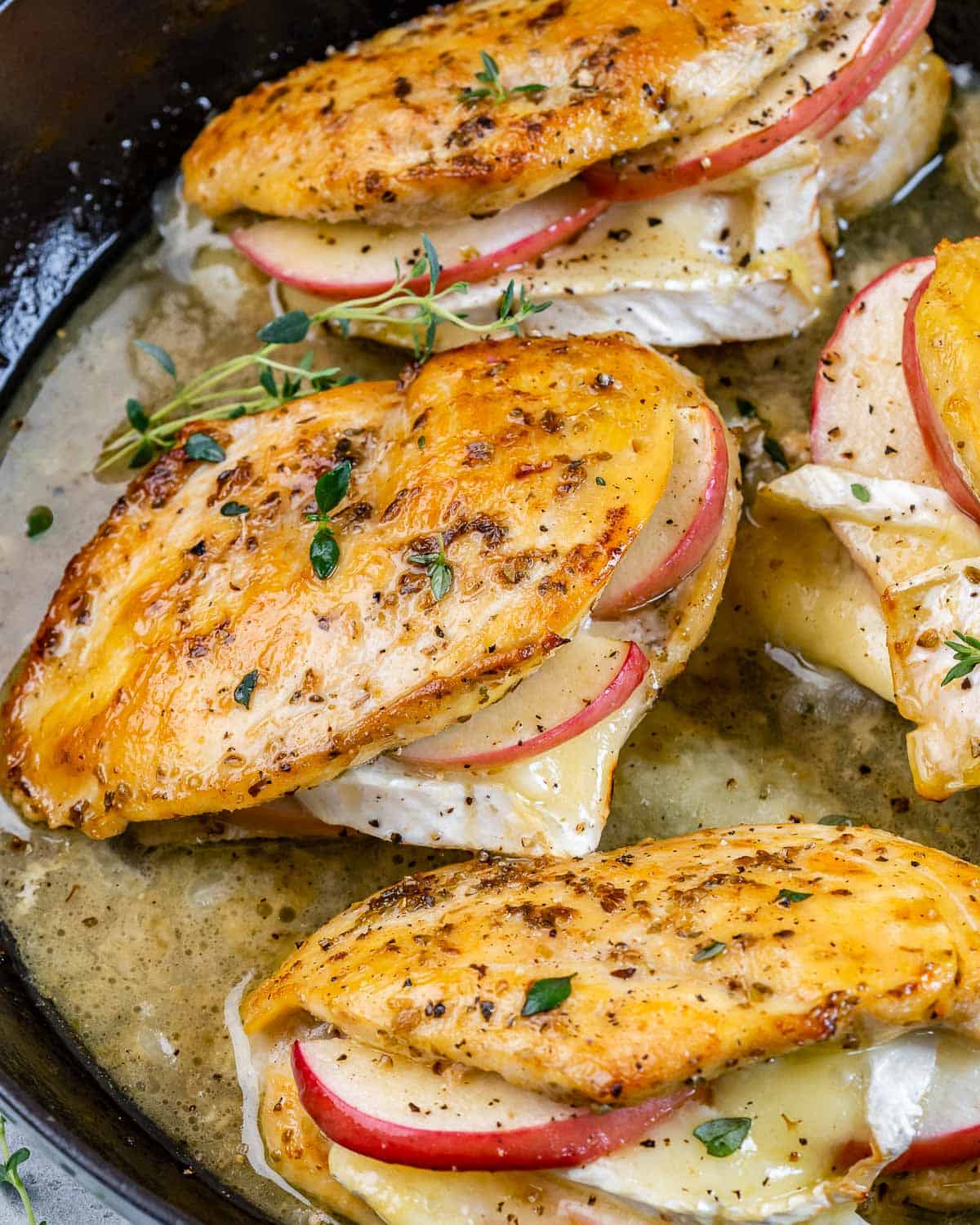 cooked chicken breasts in a pan stuffed with brie and sliced apples. 