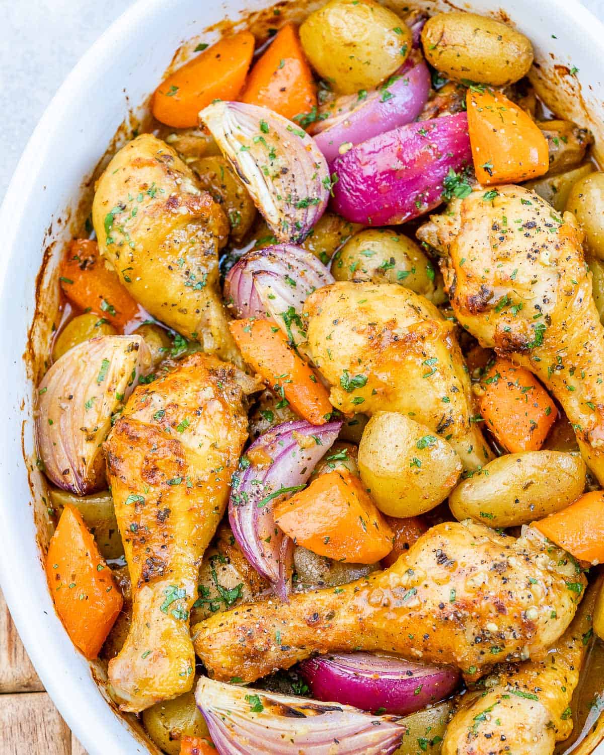 Golden-brown baked chicken legs surrounded by tender potatoes, carrots, and caramelized onions fresh from the oven.