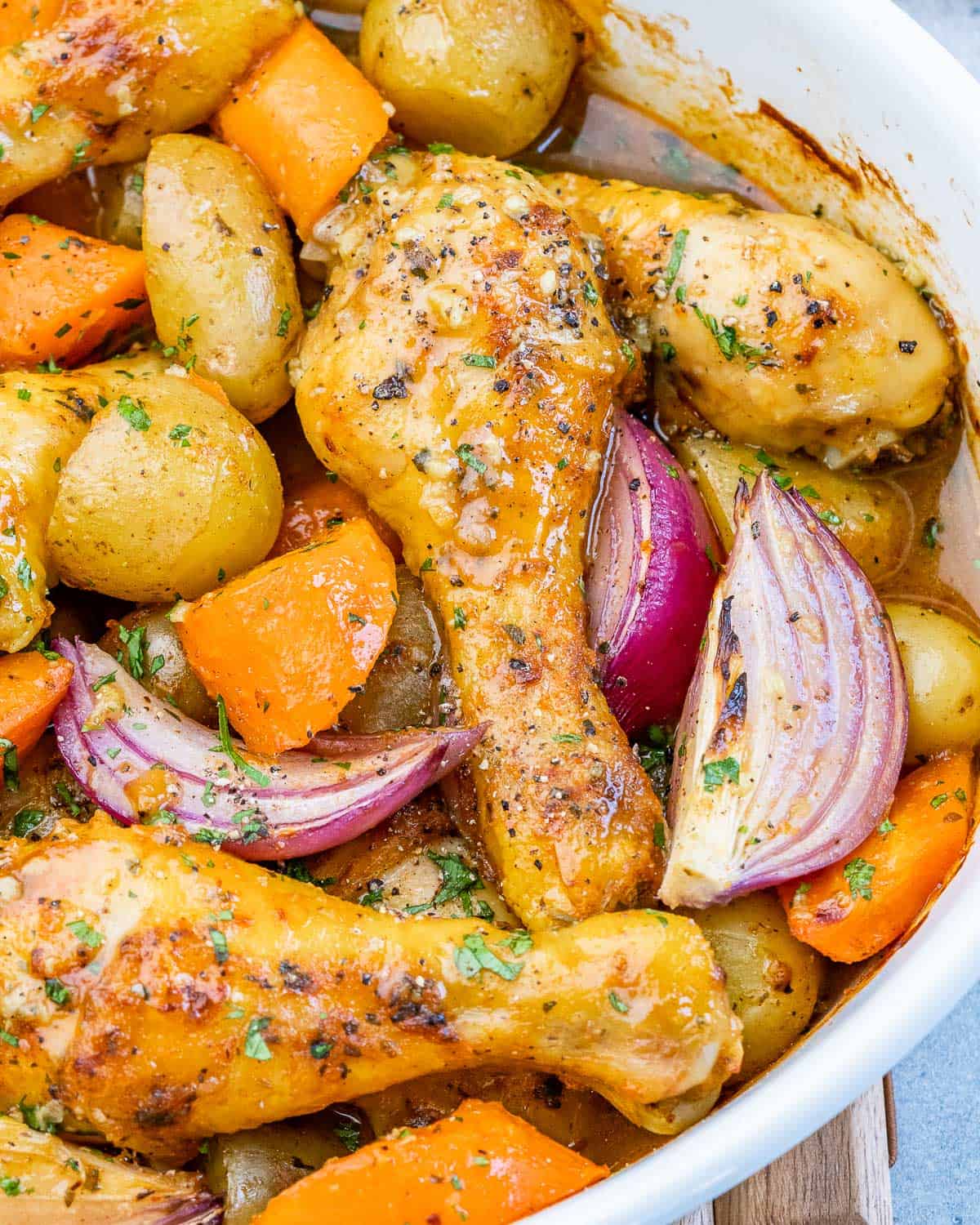 Close-up of seasoned drumsticks with potatoes and carrots, glistening after baking.