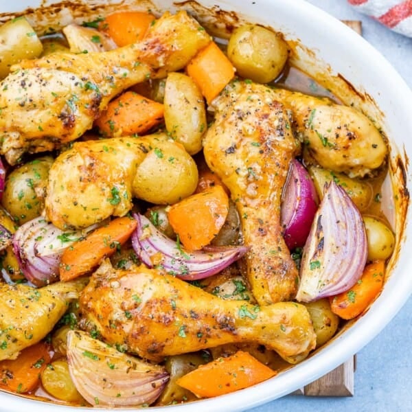 Chicken legs, baby potatoes, and red onions nestled together in a baking dish, fully coated in spices and ready to roast.