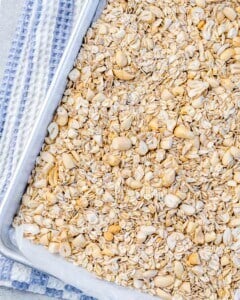 Bowl of raw whole skinned almonds, cashews, and oats on a light blue surface, ready for chopping and toasting.