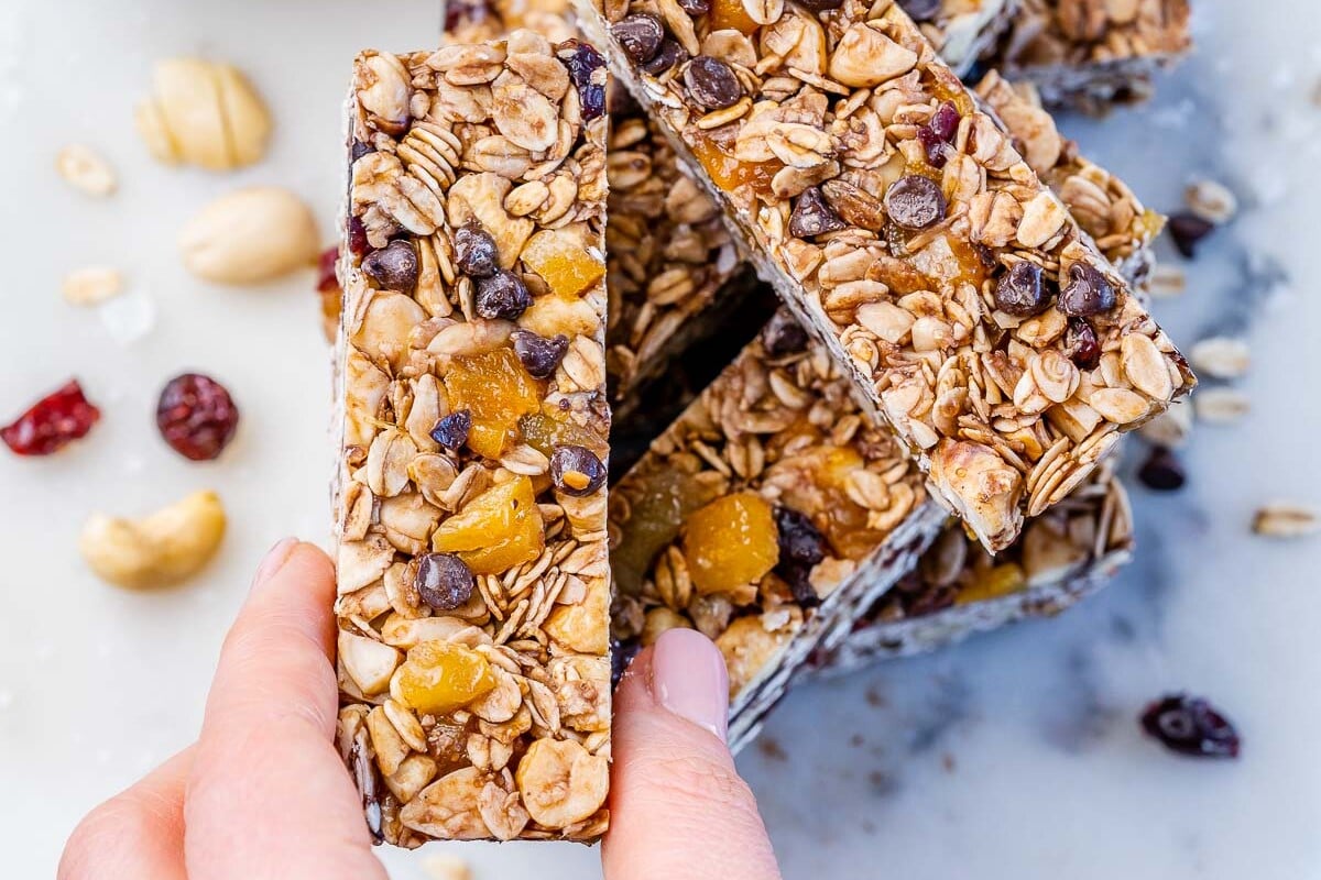 Hand holding up a healthy granola bar above a stack of granola bars.