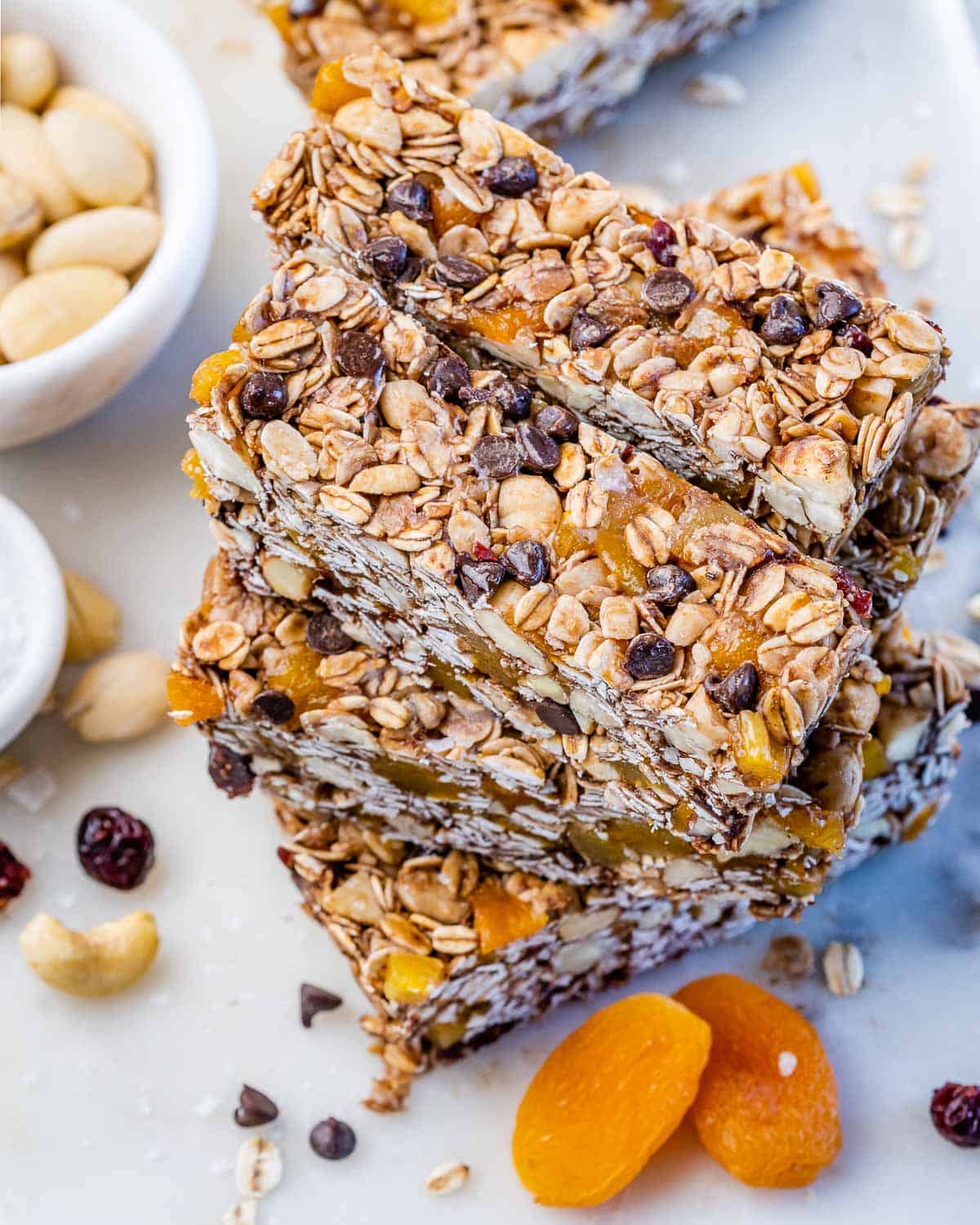 Stack of cut healthy granola bars arranged on a white surface, displaying golden toasted edges, oats, nuts, apricots, cranberries, and dark chocolate chips.