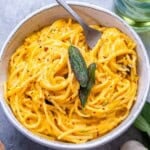 a round bowl with pumpkin spaghetti topped with a green leafy herb.
