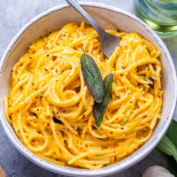 a round bowl with pumpkin spaghetti topped with a green leafy herb.