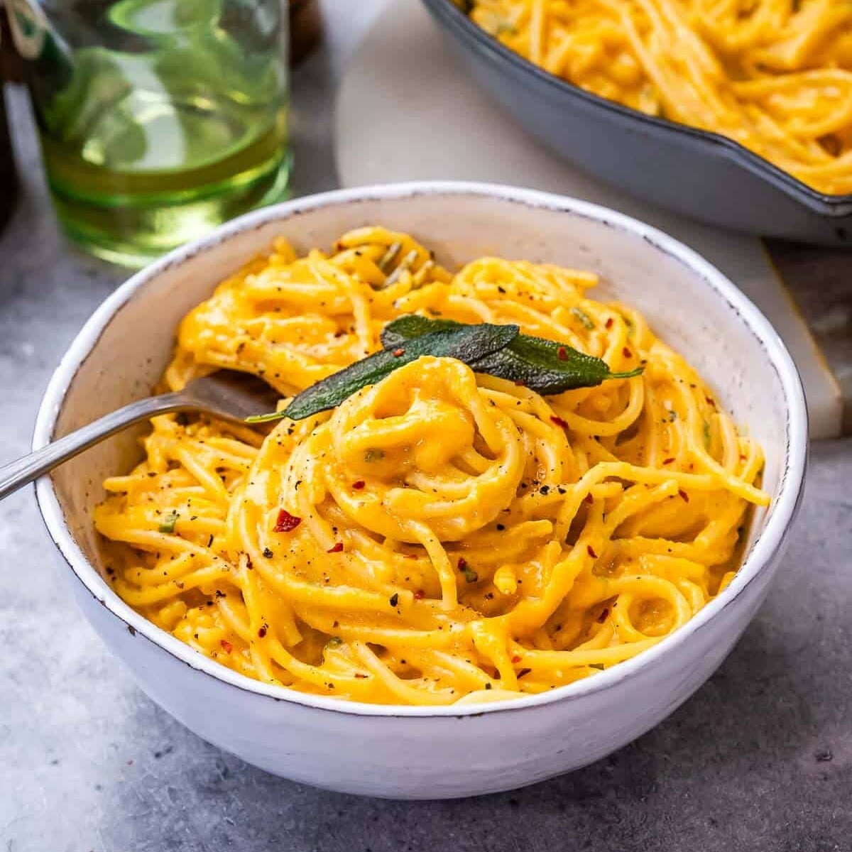 A white ceramic bowl of pumpkin alfredo pasta with a pan in the background