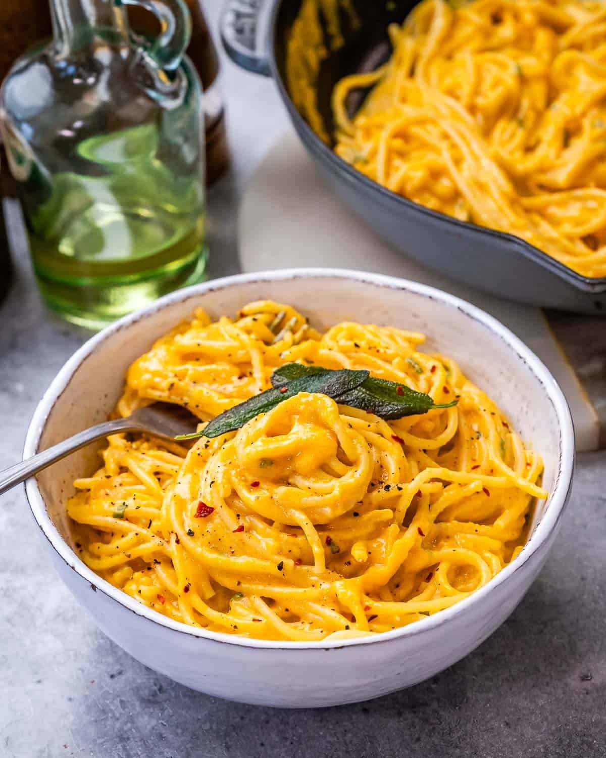 A white ceramic bowl of pumpkin alfredo pasta with a pan in the background