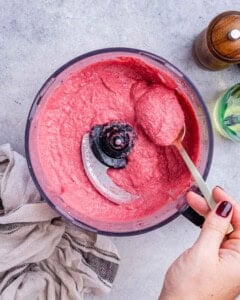 hand holding spoon and spooning some hummus from blender.