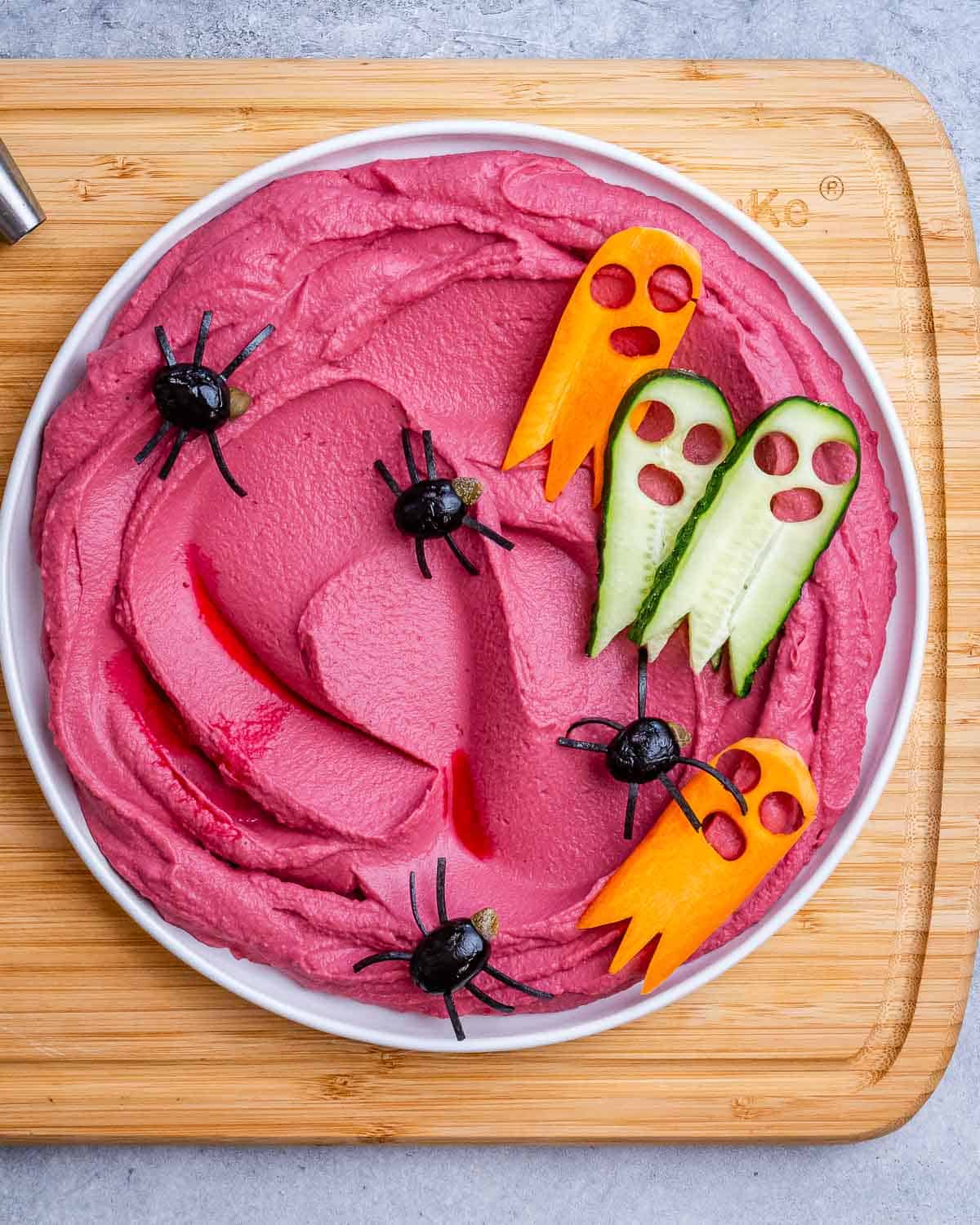 red looking hummus in a bowl topped with spider-looking olives.