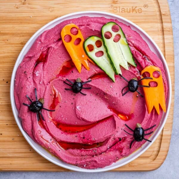 a bowl with purple hummus and spiders made out of black olives.