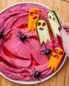 hand adding ghost veggies over beet hummus.