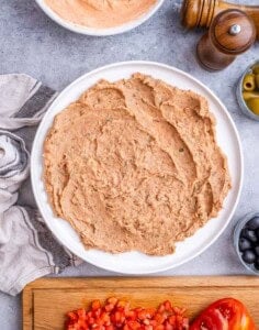 Layer of refried beans spread evenly in a round white serving dish as the base of the dip.