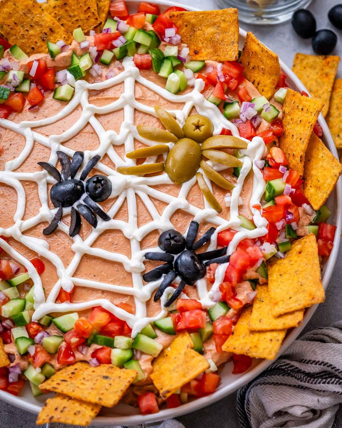 Close-up of the spider web design made with sour cream over the taco dip, with veggies around the edges.