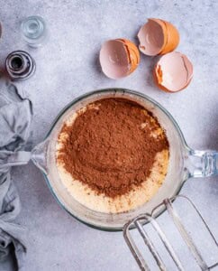 Overhead shot of dry ingredients added to wet ingredients in a mixing bowl, including cocoa powder and almond flour.
