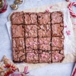Brownies cut into squares on a parchment paper topped with chopped peppermint.