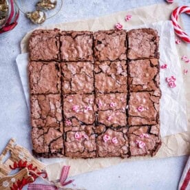 Brownies cut into squares on a parchment paper topped with chopped peppermint.