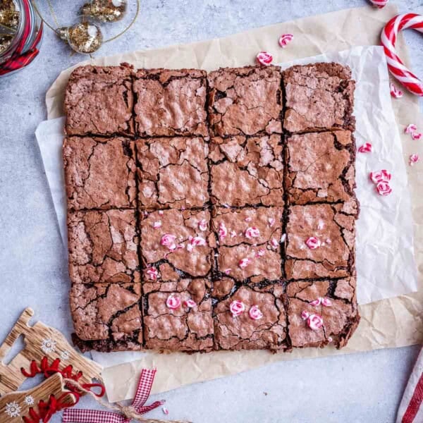 Brownies cut into squares on a parchment paper topped with chopped peppermint.
